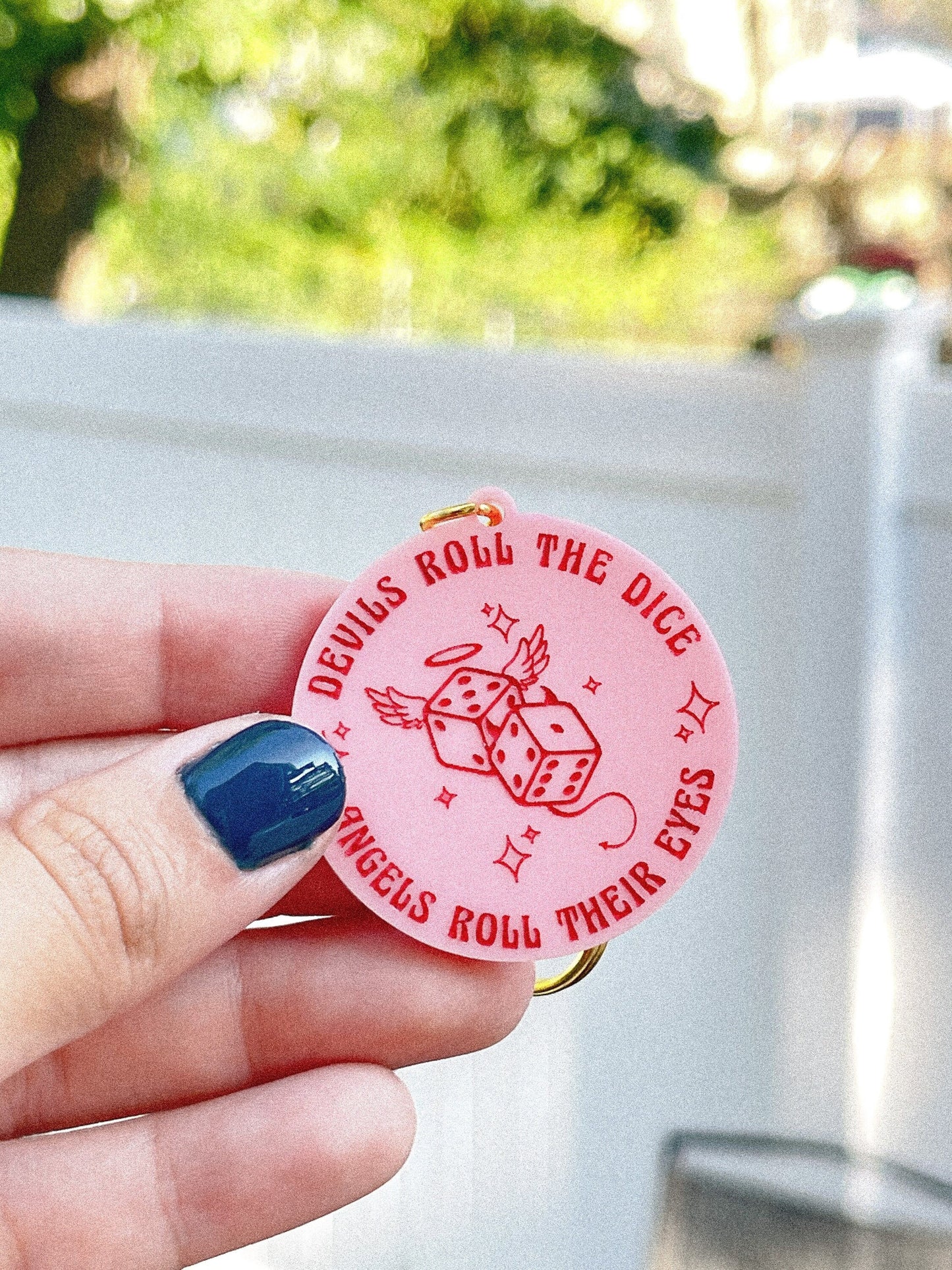 Pink circle acrylic keychain with the Taylor Swift lyrics "devils roll the dice, angels roll their eyes" engraved around dice.