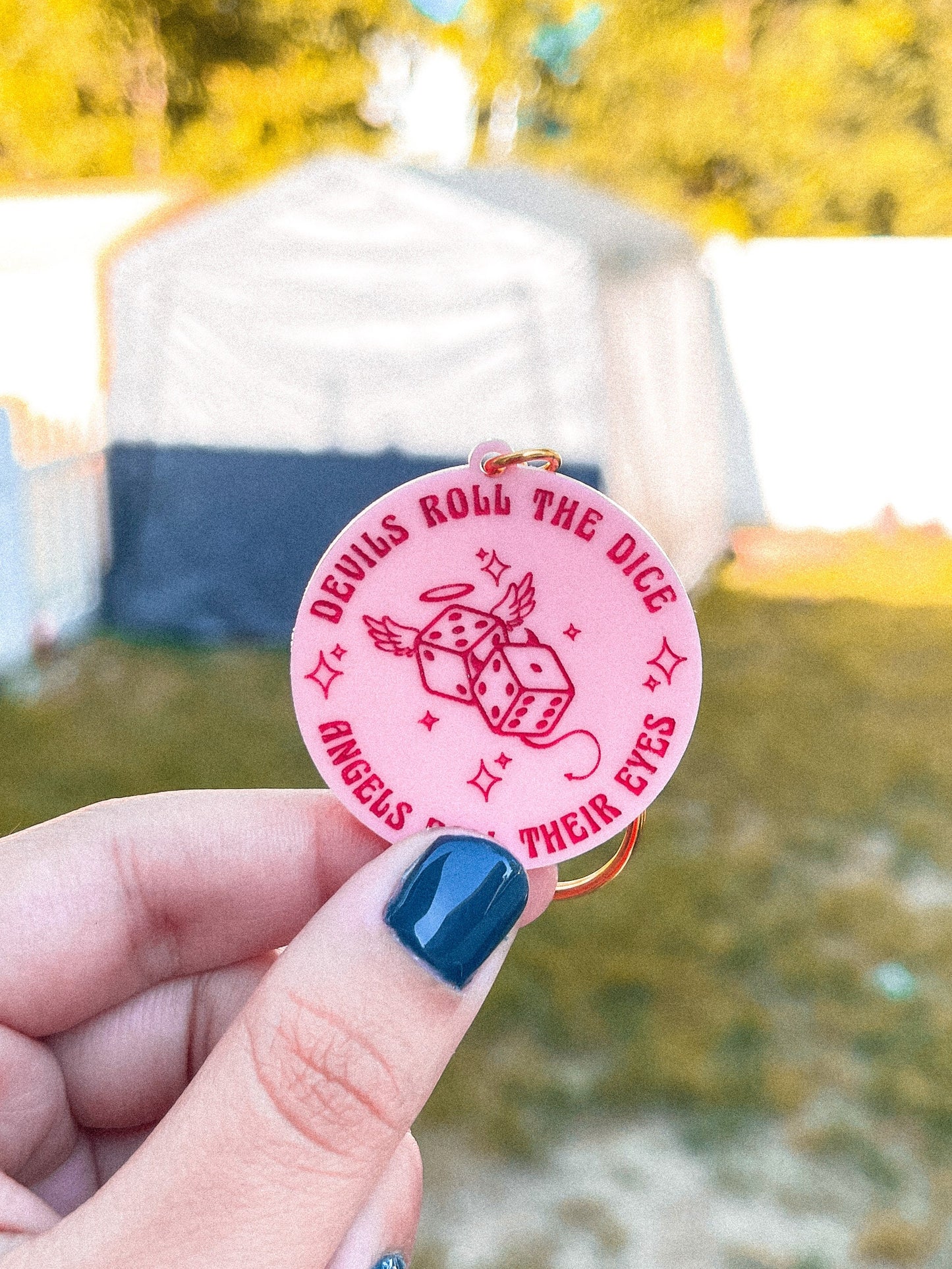 Pink circle acrylic keychain with the Taylor Swift lyrics "devils roll the dice, angels roll their eyes" engraved around dice.