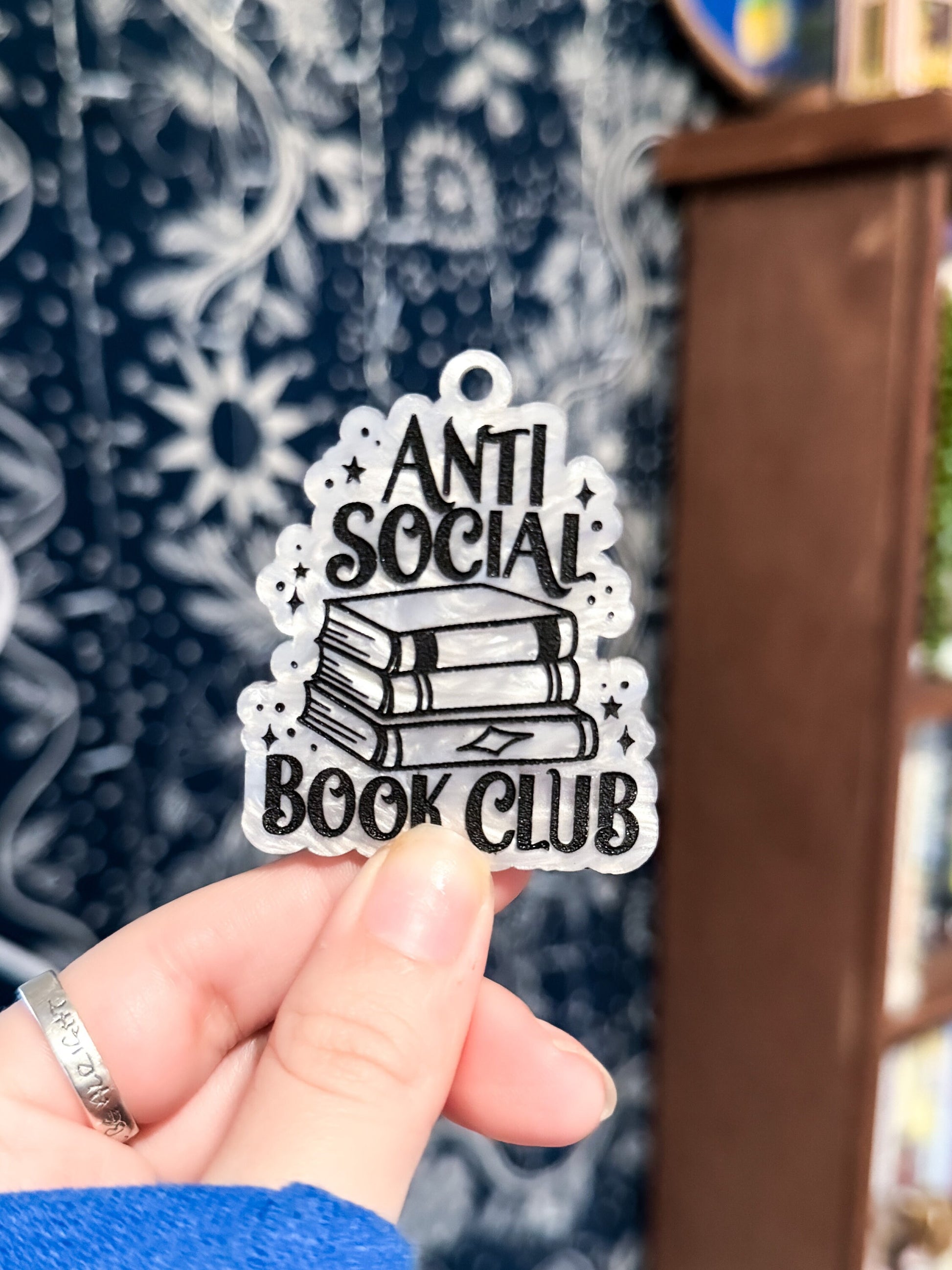 An aesthetic bookish white marble acrylic keychain with the text "anti social book club" in black. in between is a stack of books and there are sparkles scattered all around.