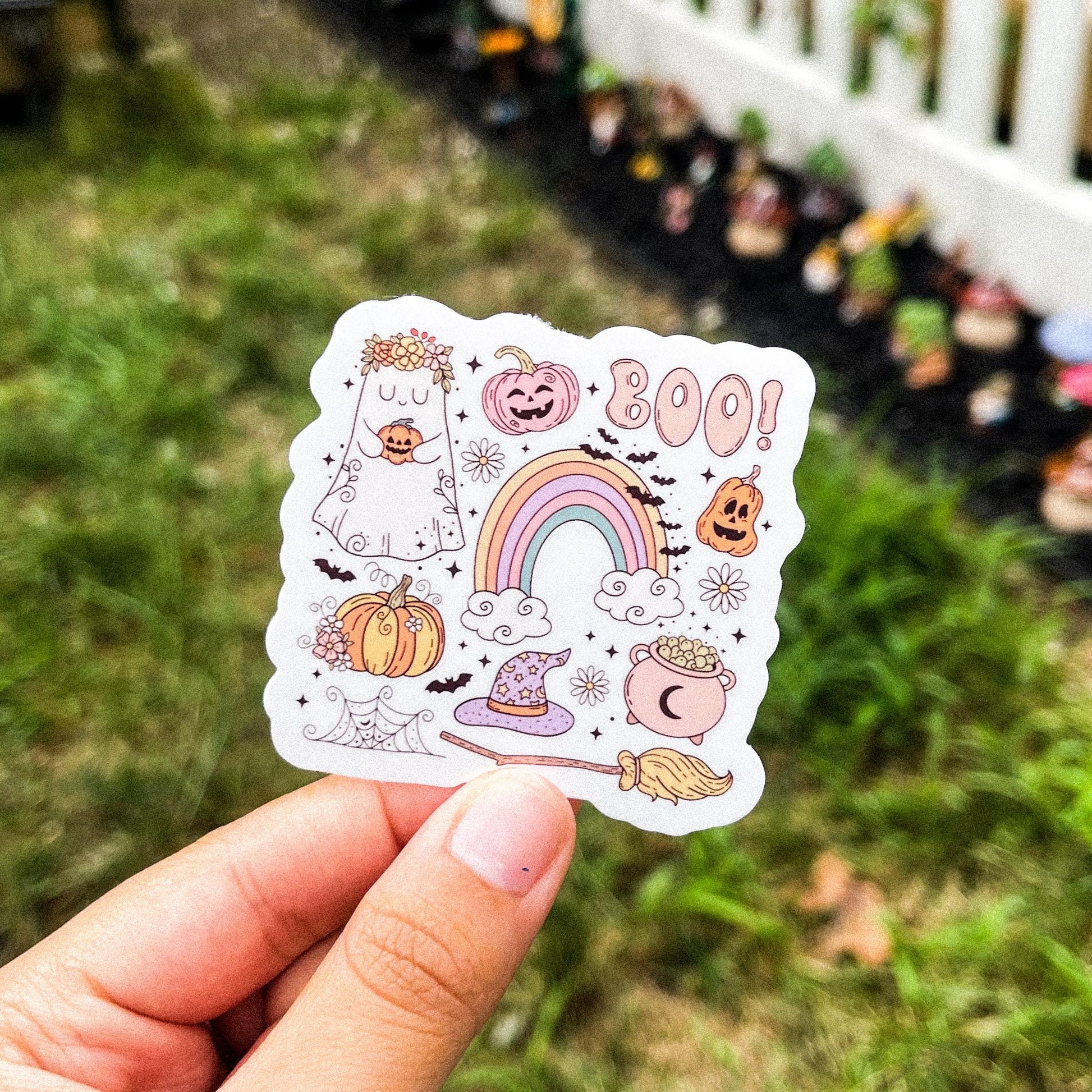 A cozy Halloween sticker with different Halloween-inspired designs such as a cauldron, broomstick, witch hat, pumpkins, ghost, a rainbow, bats, and webs. 