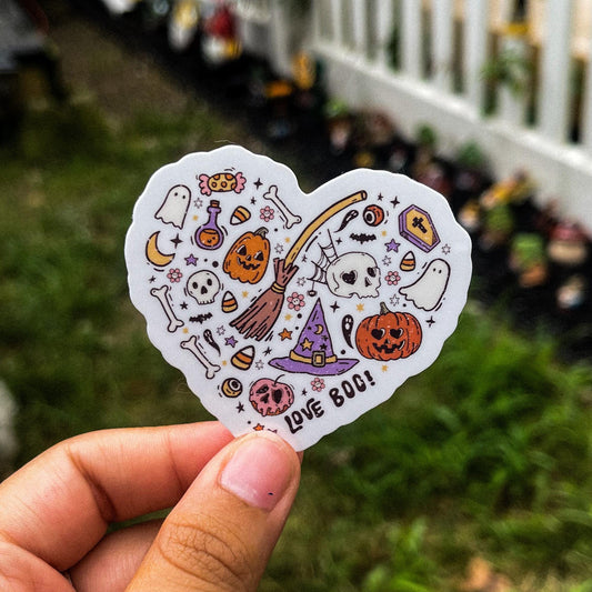 A cozy Halloween aesthetic sticker in the shape of a heart made with various Halloween-inspired doodles, including ghosts, skeletons, candy, pumpkins, and a witch hat and broomstick.