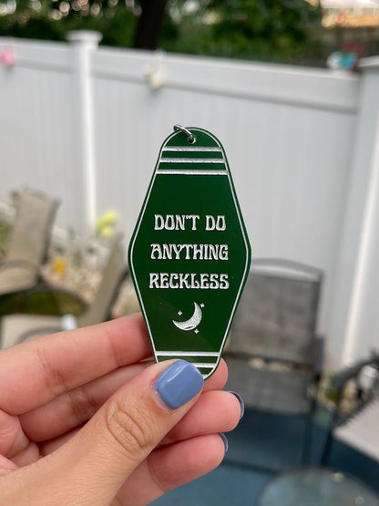 Dark green Twilight Saga inspired motel keychain with white engravings of a crescent moon and the quote "don't do anything reckless"