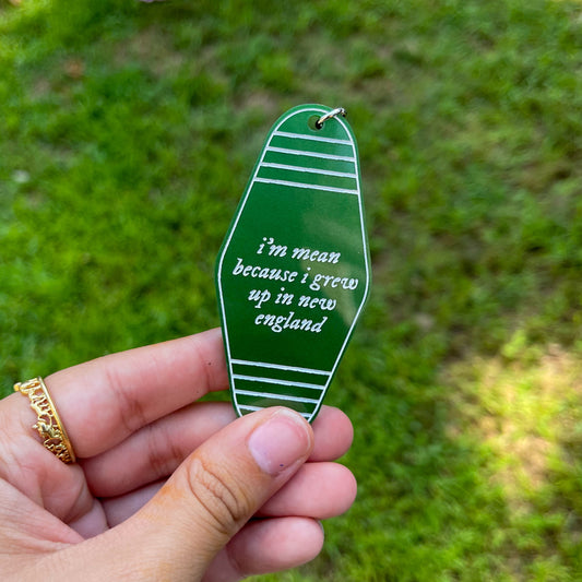 Green Noah Kahan inspired motel keychain with the lyrics "i'm mean because I grew up in New England" engraved in white. 