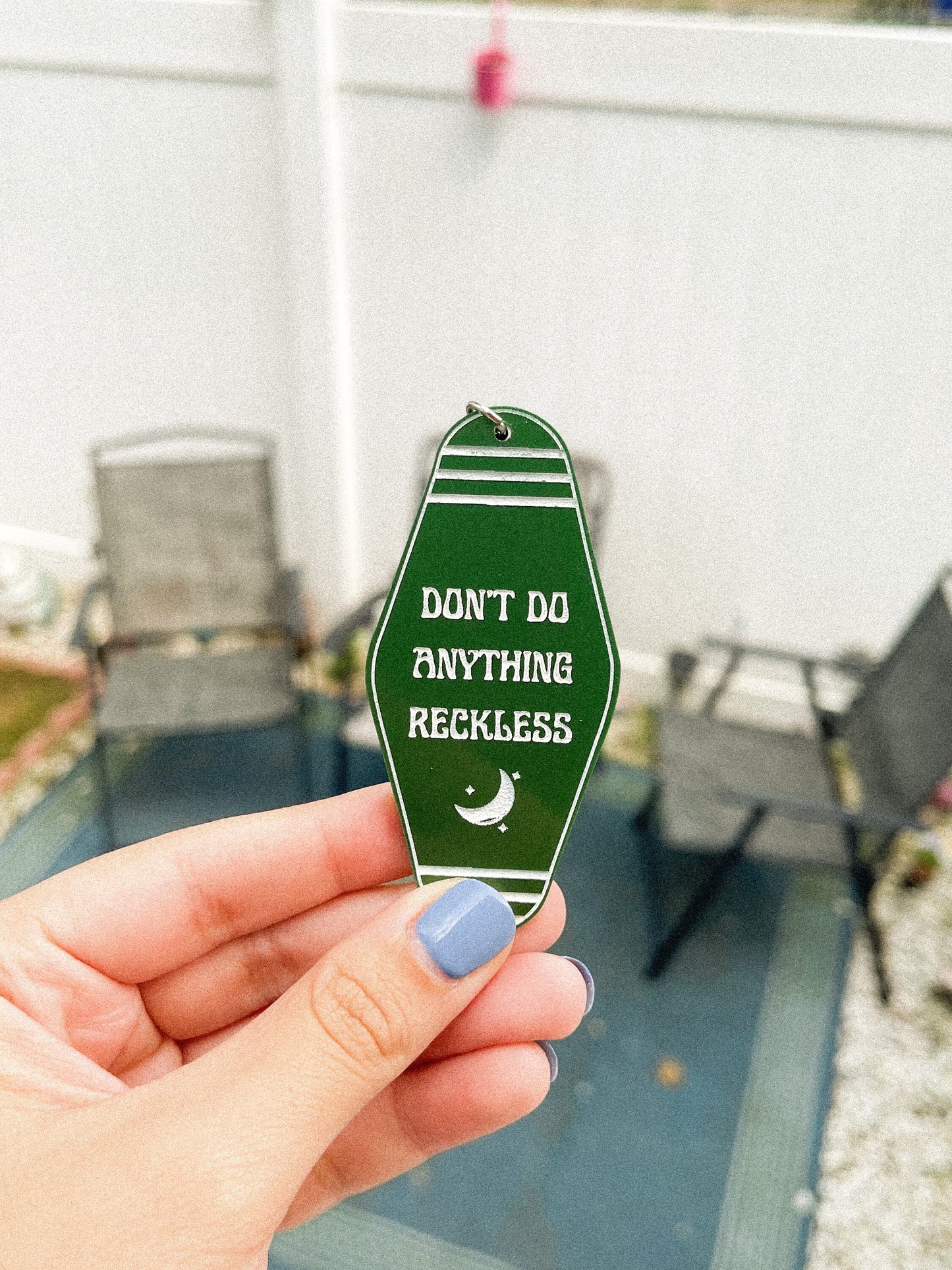 Dark green Twilight Saga inspired motel keychain with white engravings of a crescent moon and the quote "don't do anything reckless"