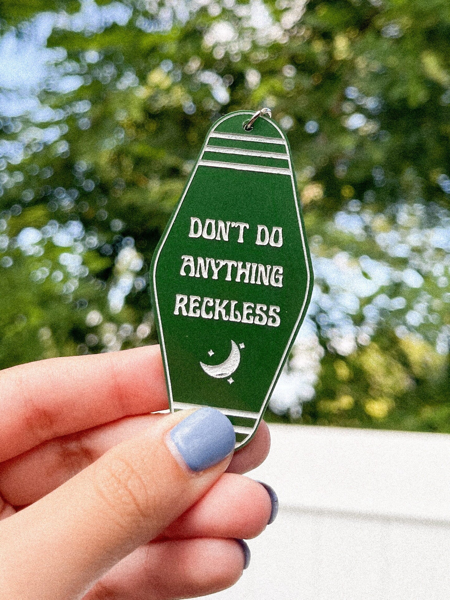 Dark green Twilight Saga inspired motel keychain with white engravings of a crescent moon and the quote "don't do anything reckless"