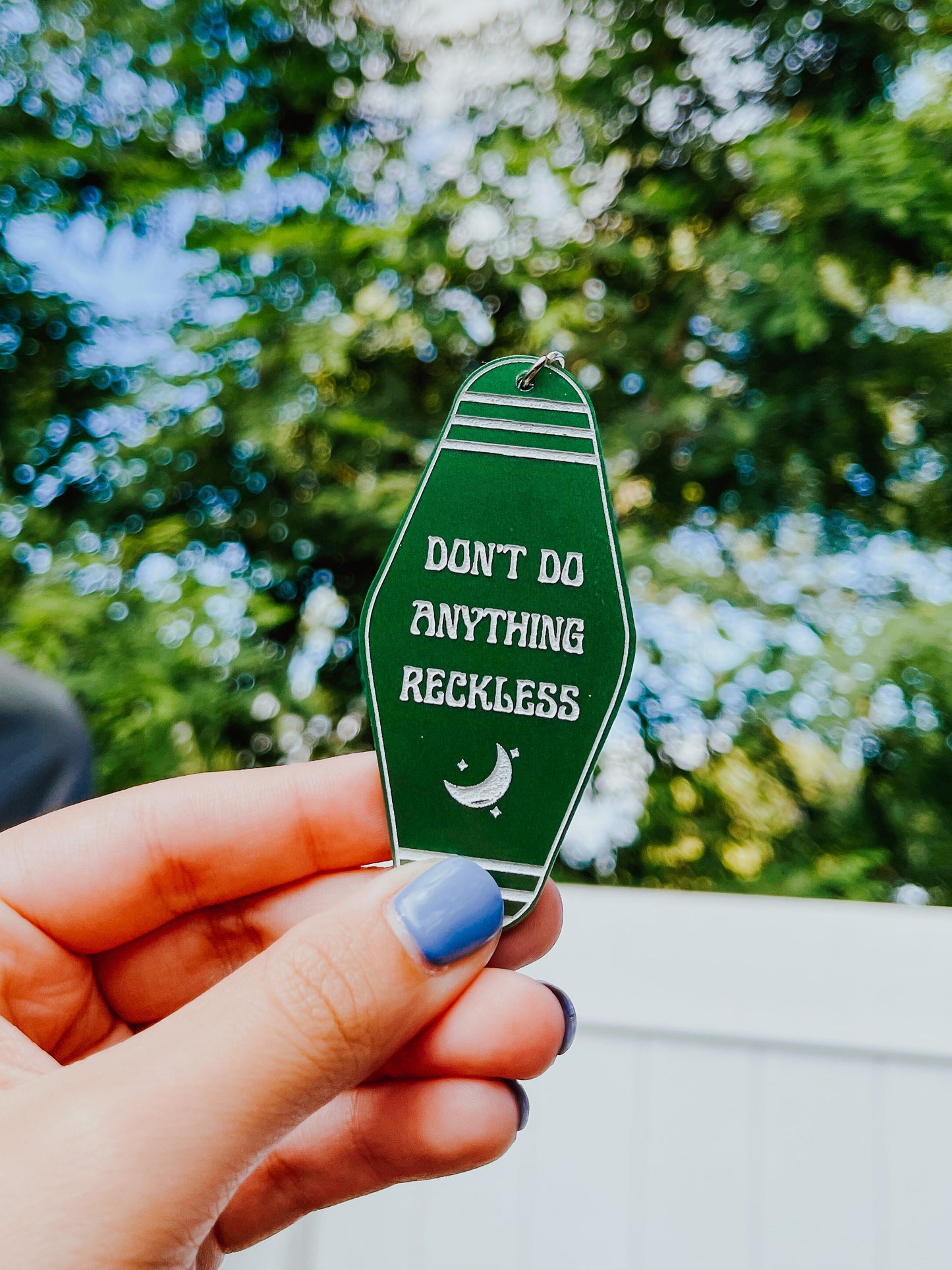 Dark green Twilight Saga inspired motel keychain with white engravings of a crescent moon and the quote "don't do anything reckless"