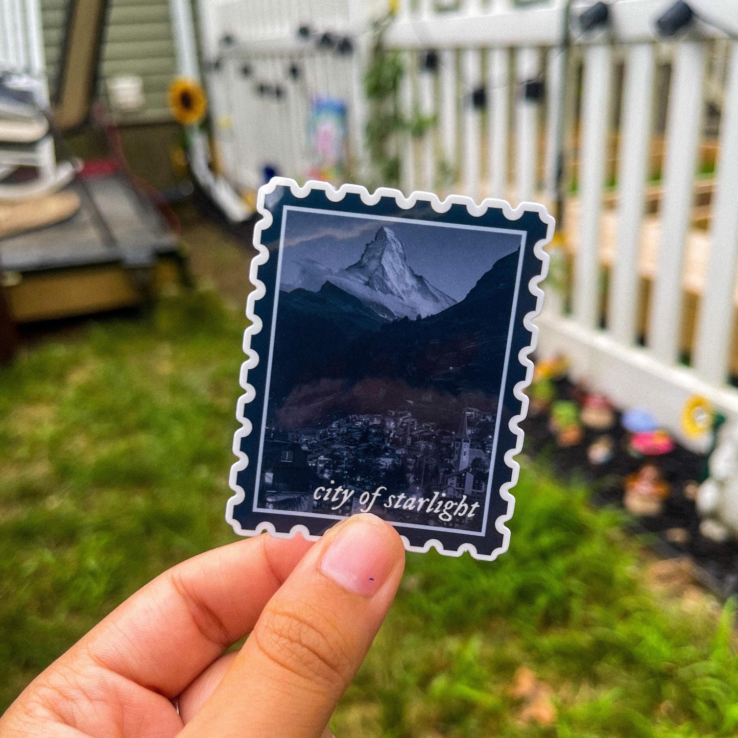 Sticker in shape of postage stamp with a mountain city and the words "city of starlight" inspired by ACOTAR's Velaris