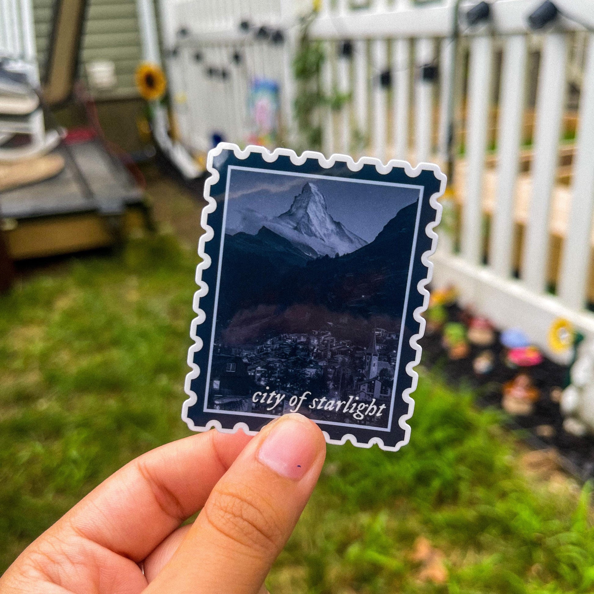 Sticker in shape of postage stamp with a mountain city and the words "city of starlight" inspired by ACOTAR's Velaris